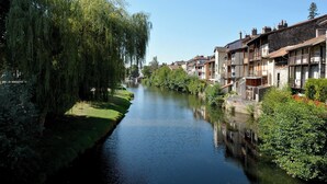 Een smalle rivier met gebouwen aan één kant en een wilg aan de overkant.
