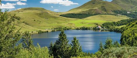 A lake surrounded by green hills and trees, with a house visible in the distance.