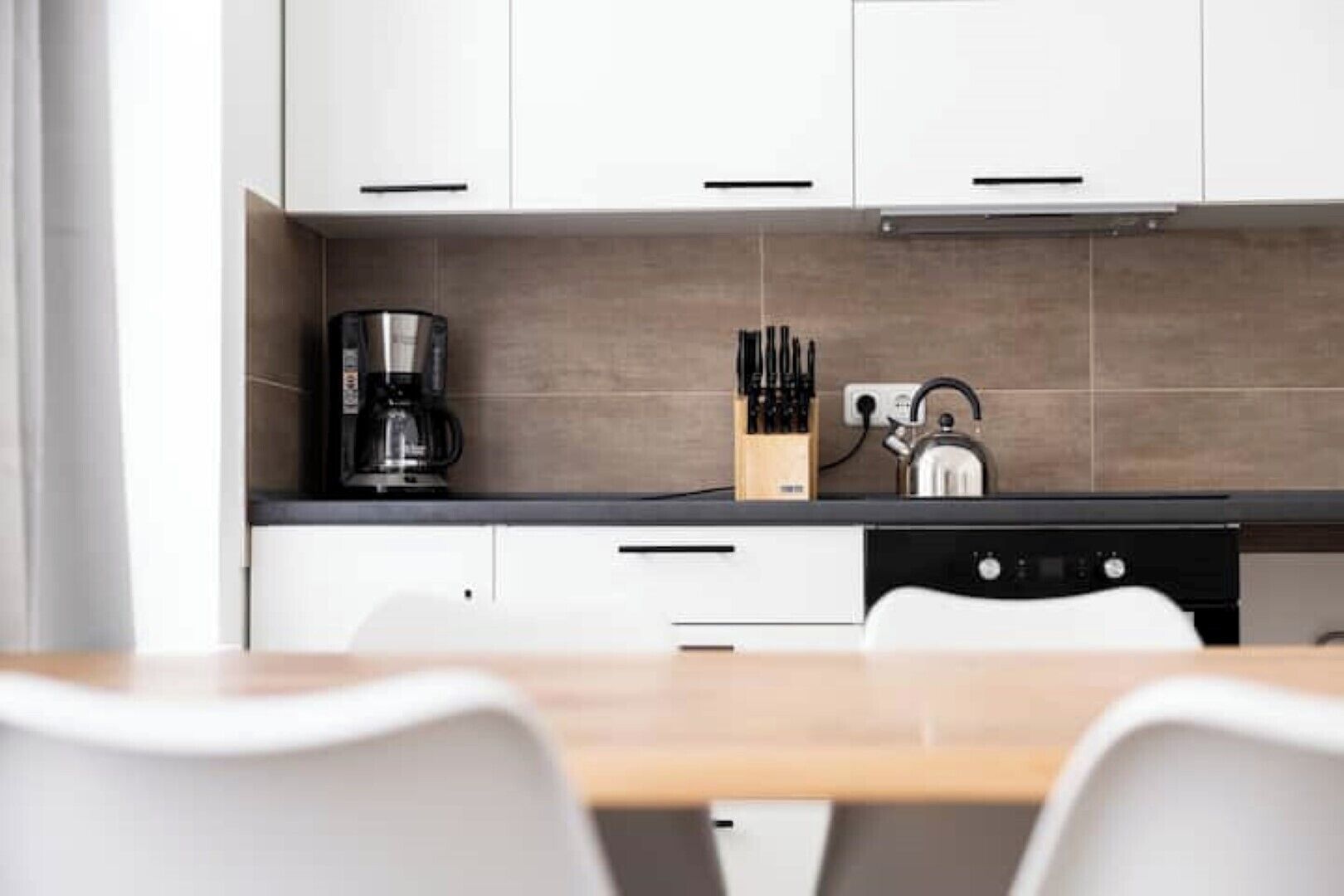 A modern kitchen with white cabinets, a black countertop, and a wooden dining table.