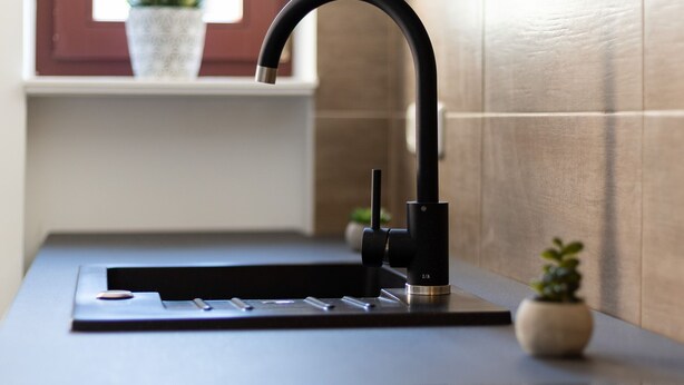 Una cocina moderna con un grifo negro elegante, un lavamanos de acero inoxidable y una ventana con una planta en maceta.