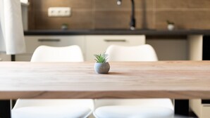 Una cocina moderna con una mesa de madera, sillas blancas y una pequeña planta en maceta.
