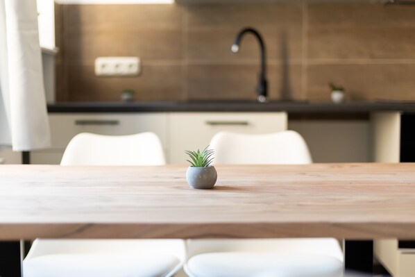 A modern kitchen with a wooden table, white chairs, and a small potted plant.