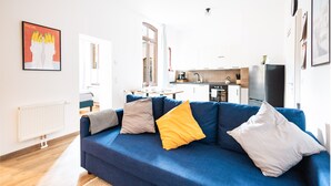 Una sala moderna con un sofá azul, un radiador y una cocina al fondo.