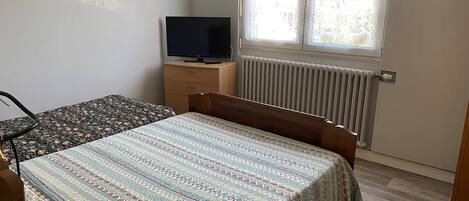 Ein Schlafzimmer mit Bett, Kommode, Fernseher und einem Fenster mit Jalousien.