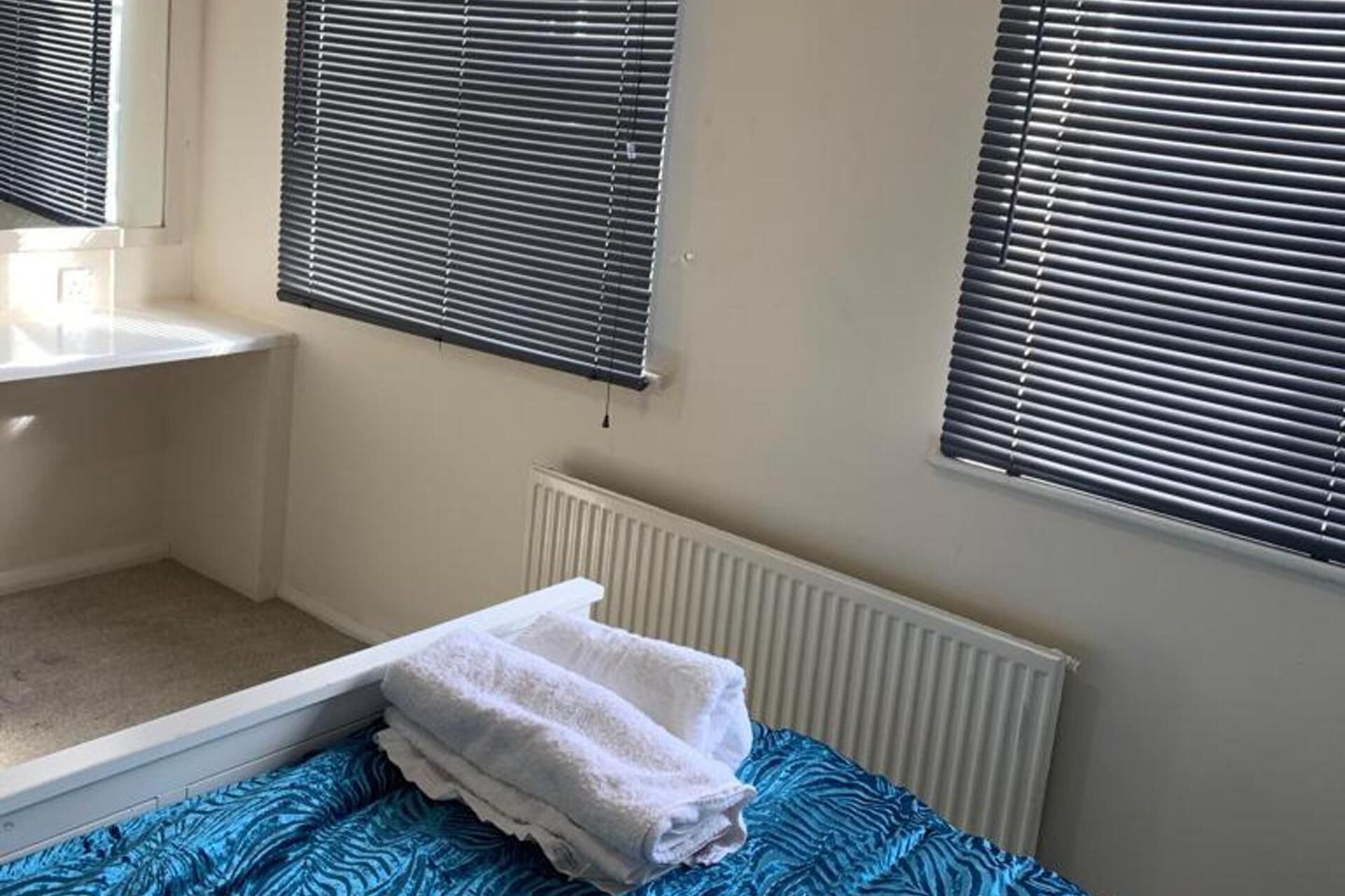 A bathroom with a bathtub, a white radiator, and two windows with blinds.