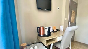 A hotel room with a wooden desk, a coffee machine, a kettle, a TV mounted on the wall, and a door with a sign. - Le Gîte des Voyageurs  (Bourbourg)