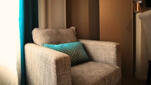 A corner armchair with a patterned cushion, positioned next to a wall with a lamp. - Le Gîte des Voyageurs  (Bourbourg)