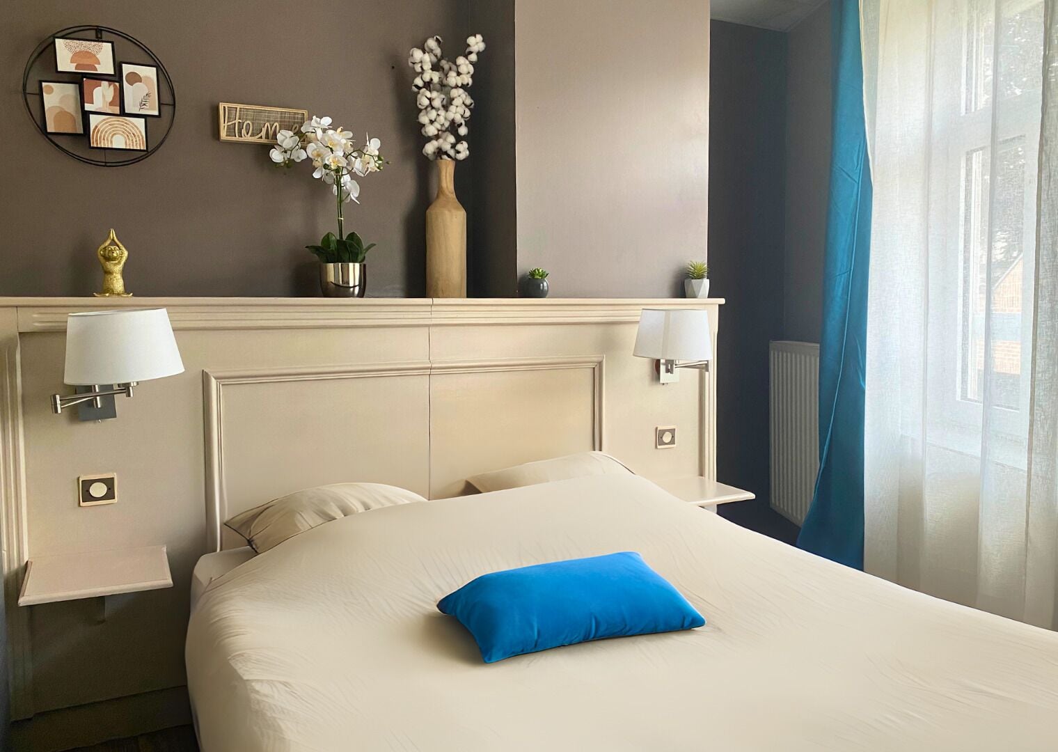 Hotelkamer met een bed, twee nachtkastjes, een wandlamp, een decoratieve vaas met bloemen en een lijst met kunstwerk.