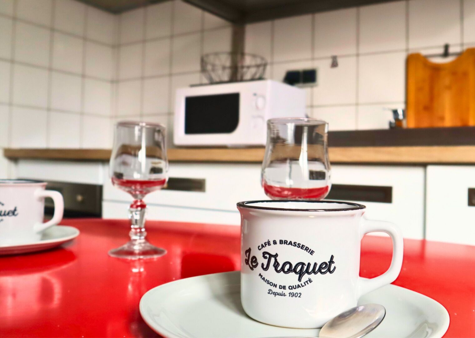 A kitchen with a red countertop, a white mug with text, and two wine glasses.