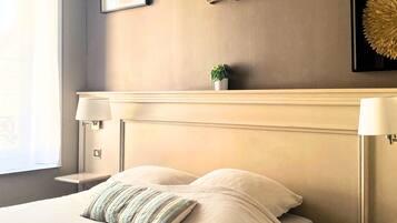 A neatly arranged bedroom with a large bed, two bedside lamps, a small potted plant, and a framed artwork on the wall.