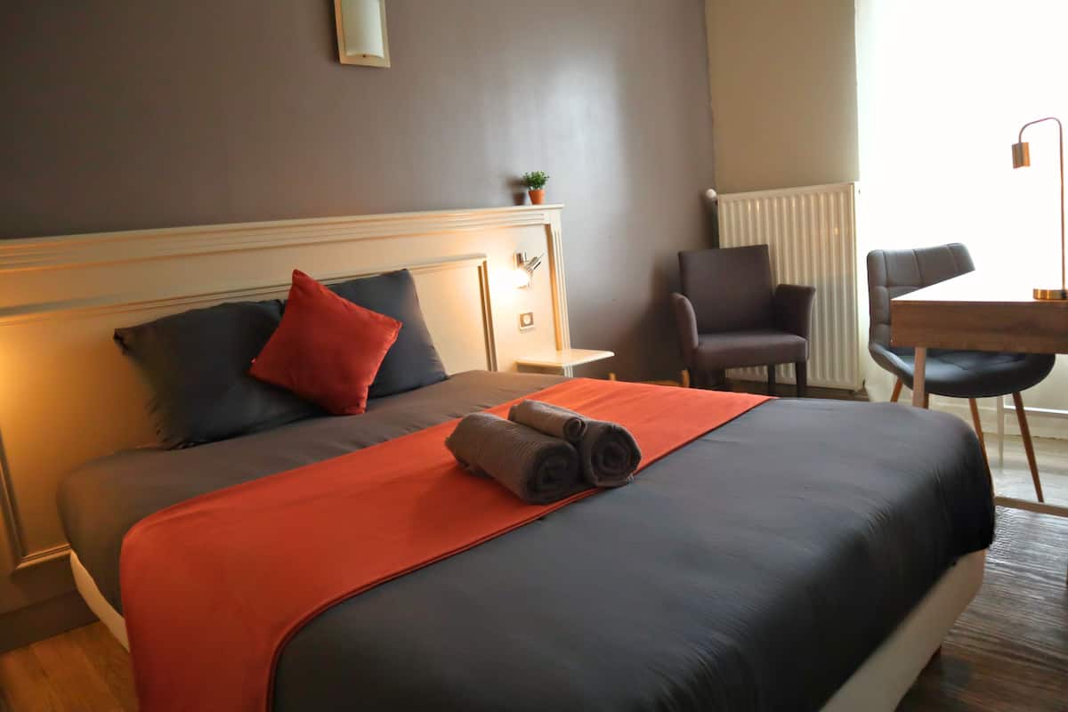 Habitación de hotel con cama, mesita de noche, silla, escritorio y radiador.
