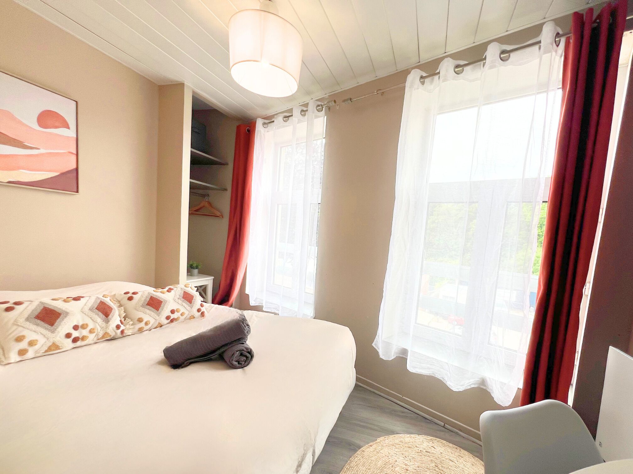 A bedroom with a large bed, a bedside table, a chair, and a window with curtains.