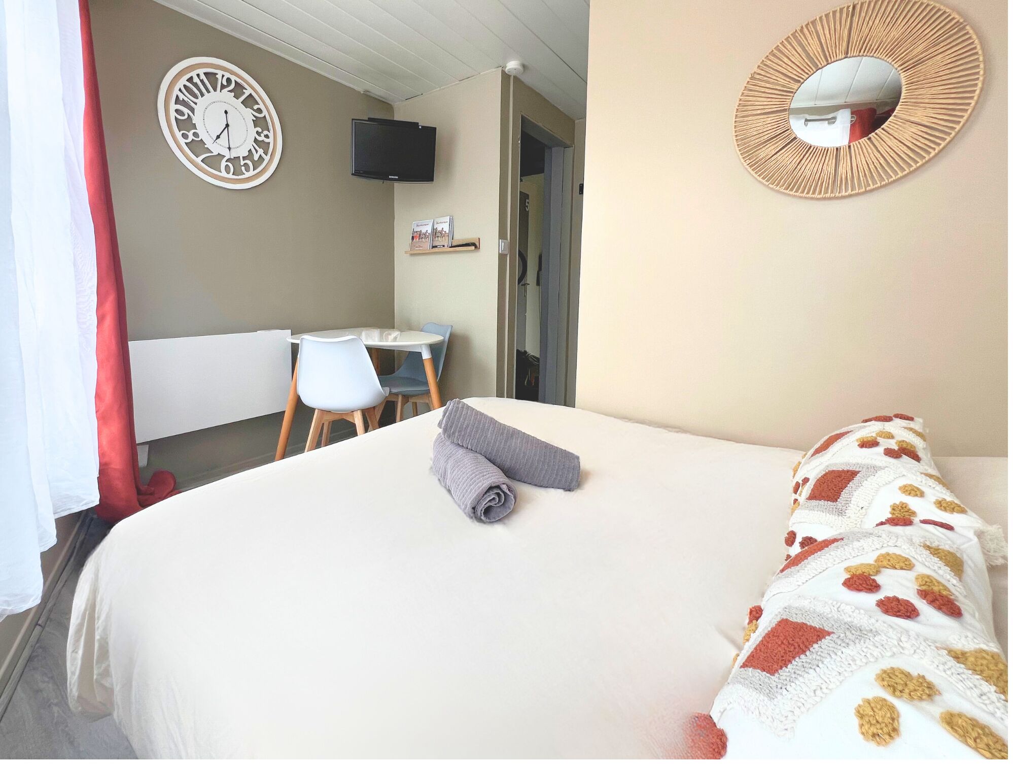 A hotel room with a bed, a desk with a chair, a television, and a clock on the wall.