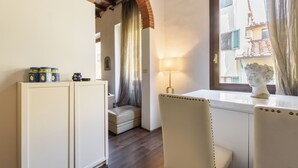 A compact room with a wooden floor, a white sofa, a small table with a lamp, and a window with a view of buildings. - Borgo Art Apartment by Mmega (Florence)