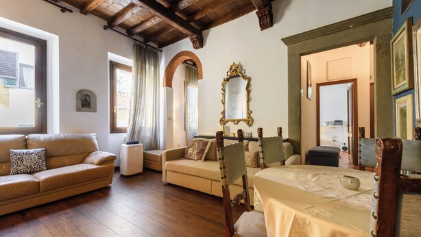 A spacious living room with wooden flooring, a sofa, a chair, and a table. - Borgo Art Apartment by Mmega (Florence)