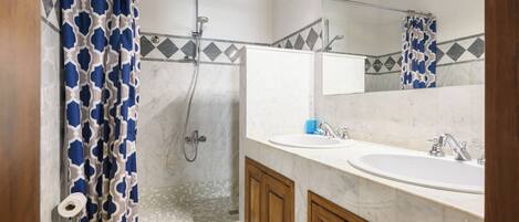 A bathroom with a shower, toilet, two sinks, and wooden cabinets.