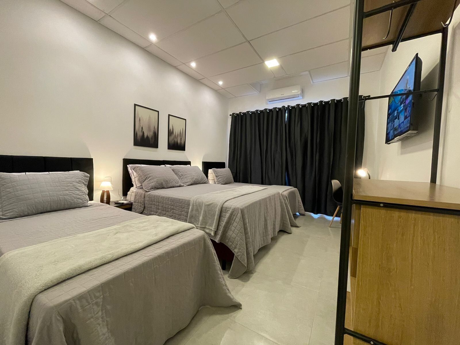 Ett hotellrum med två sängar, ett skrivbord, en stol, en TV och ett fönster med gardiner.
