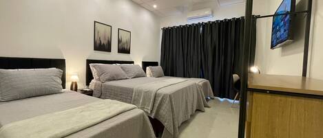 Ein Hotelzimmer mit zwei Betten, einem Schreibtisch, einem Stuhl, einem Fernseher und einem Fenster mit Vorhängen.