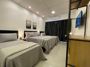 A hotel room with two beds, a desk, a chair, a TV, and a window with curtains. - VILLA BILAC 08 (Blumenau)