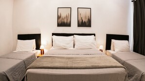 Una habitación de hotel con dos camas individuales, una cama grande, una mesita de noche con una lámpara y dos cuadros en la pared.