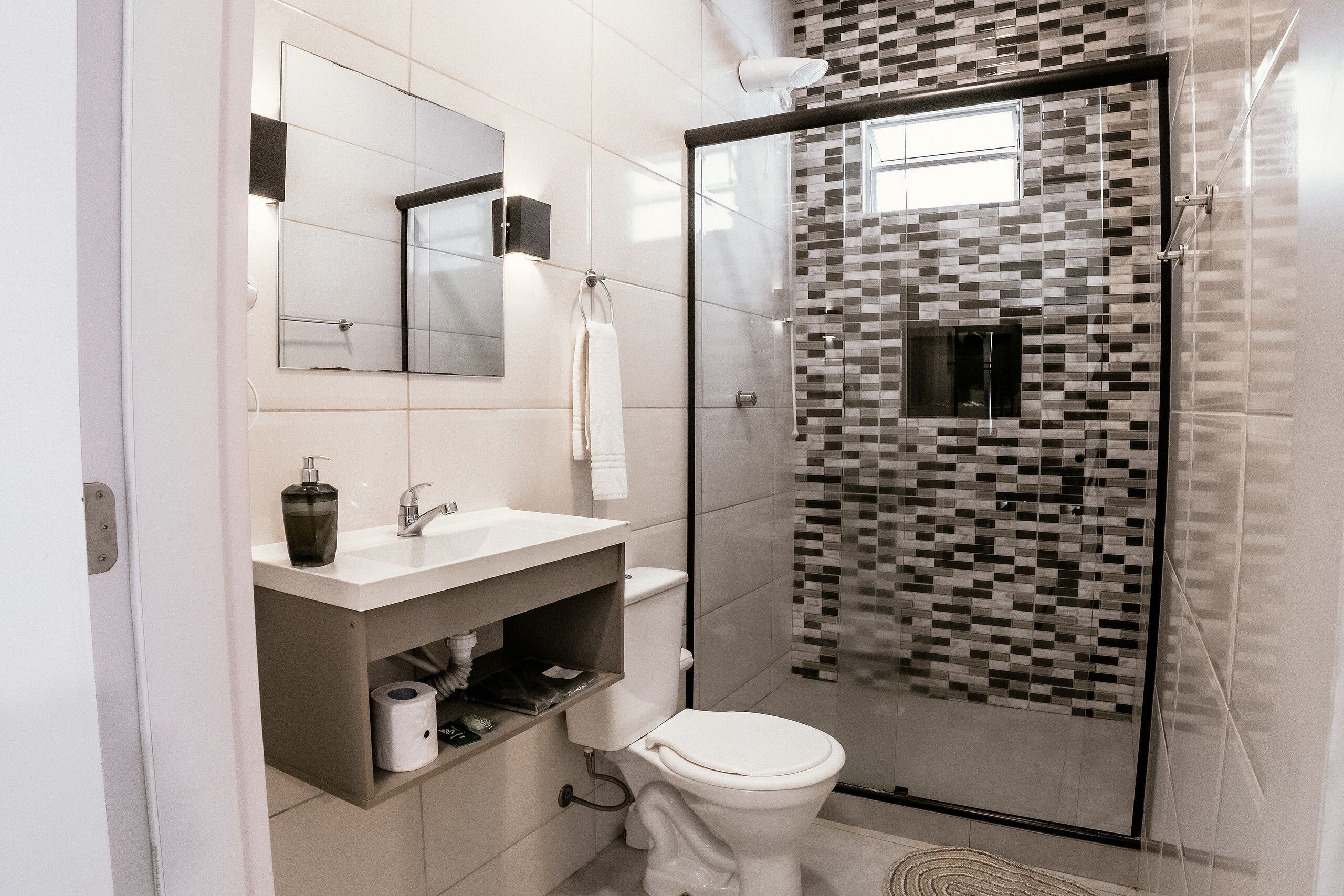 Un baño moderno con cabina de ducha de vidrio, inodoro blanco, lavamanos con espejo y salpicadero de azulejos.
