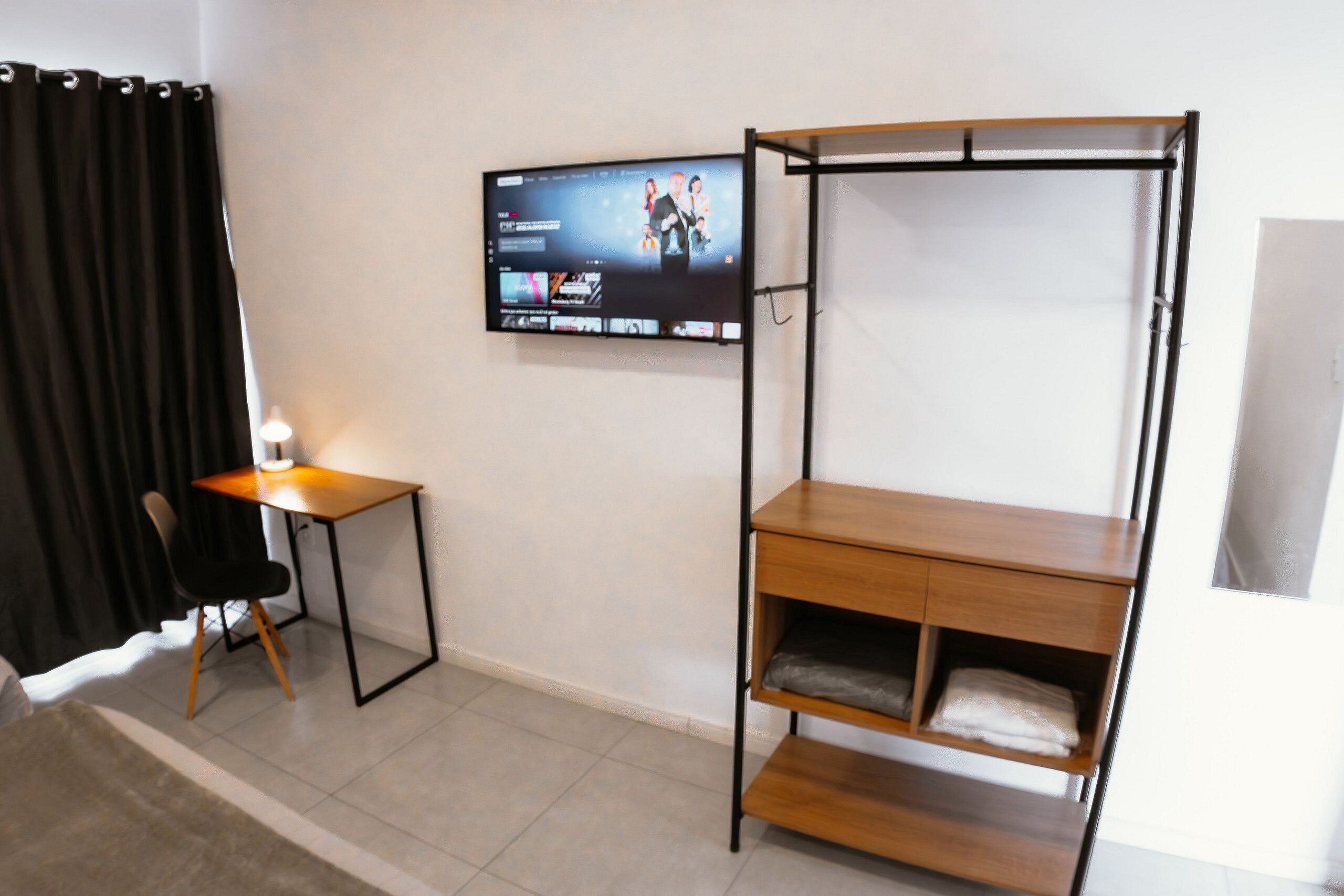 Une pièce comprenant un lit, un bureau, une chaise, un téléviseur fixé au mur et une fenêtre.