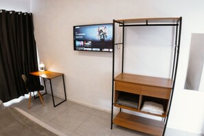 Quarto com cama, escrivaninha, cadeira, televisão na parede e janela.