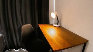 A wooden desk with a lamp, a black chair, and a black curtain in a room.