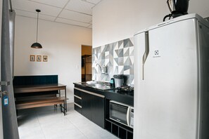 A modern kitchen with a refrigerator, oven, and sink. There is a bench and a hanging light fixture. - VILLA BILAC 08 (Blumenau)