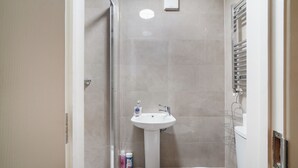 A small, modern bathroom with a pedestal sink, a toilet, and a glass shower enclosure. - Prime Central London Private Studio Apartment (London)