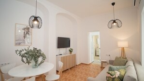 A modern living room with a grey sofa, a dining table with chairs, a TV mounted on the wall, and two pendant lights. - SibsSanlucar Duquesa - Ideal Parejas (Sanlúcar de Barrameda)