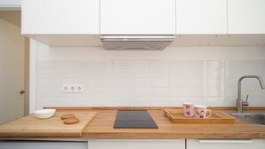 A modern kitchen with white cabinets, a wooden countertop, a black cutting board, a white bowl, a wooden tray, and a stainless steel sink. - SibsSanlucar Duquesa - Ideal Parejas (Sanlúcar de Barrameda)