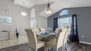 Un comedor con una mesa de vidrio, sillas tapizadas en color beige y un alfombra azul con estampado.