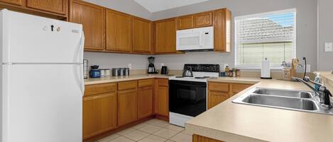 A kitchen with wooden cabinets, a white refrigerator, a microwave, a stove, and a sink.