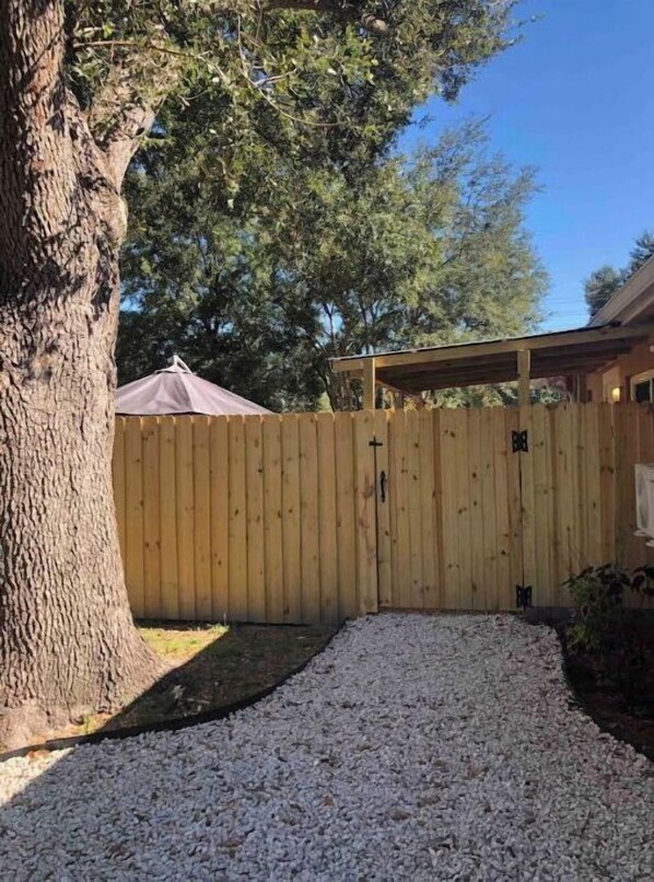 A wooden fence with a gate, a tree, and a covered patio area.