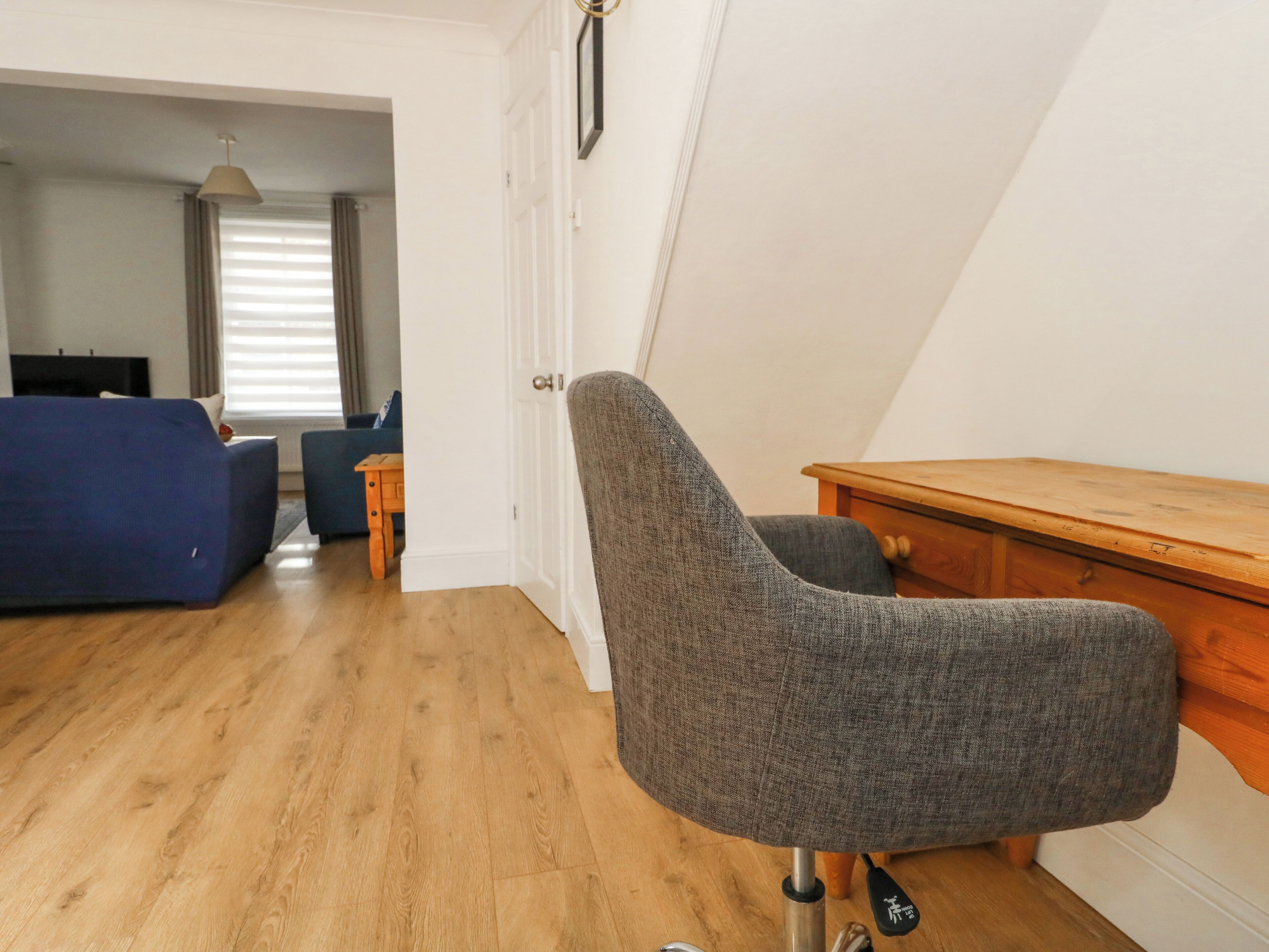 A modern living room with a grey armchair, wooden desk, and a blue sofa.
