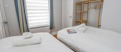 A hotel room with two beds, a wooden wardrobe, a window with curtains, and a door.