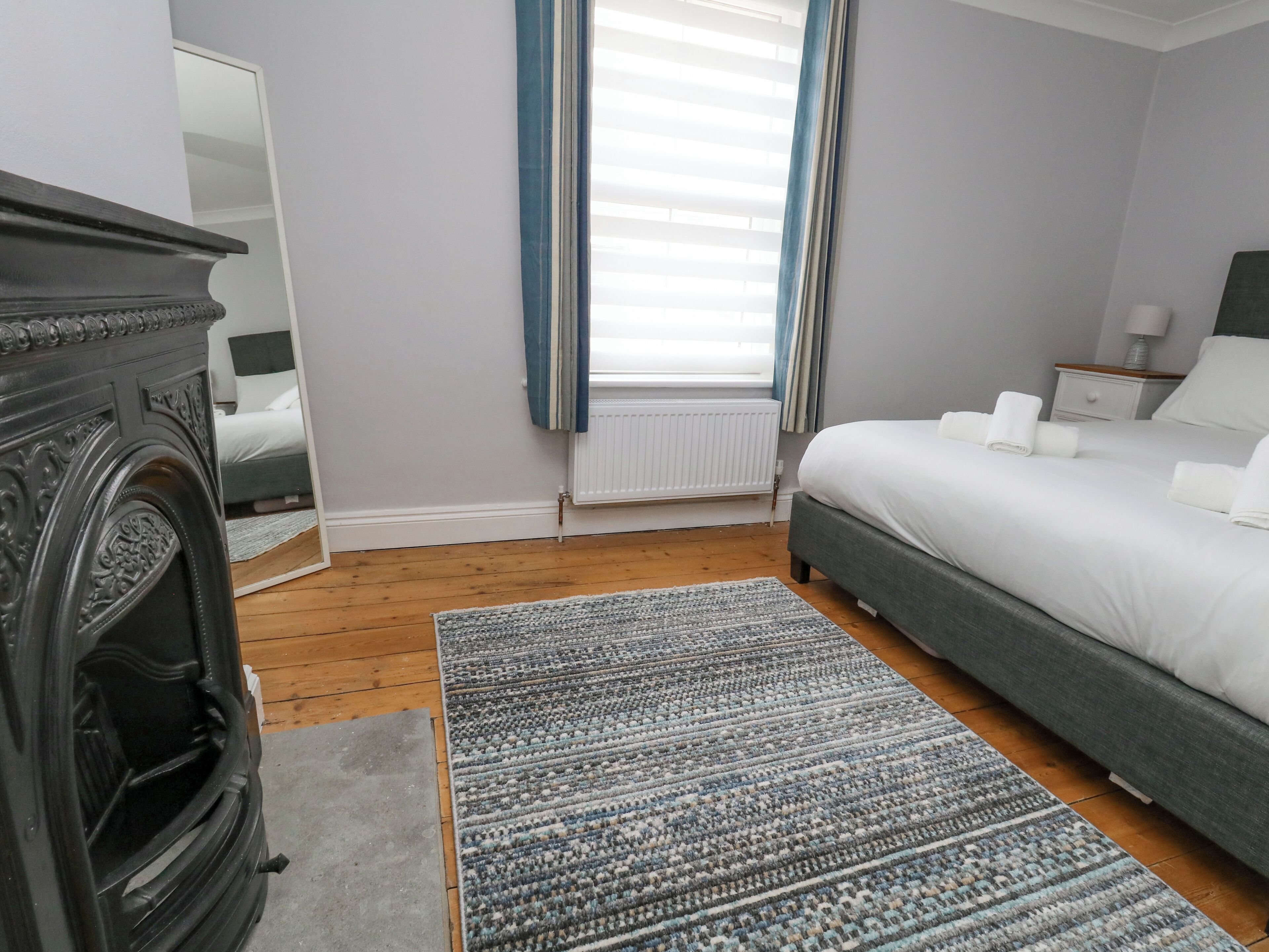Un dormitorio con cama, cómoda, radiador y ventana con cortinas.