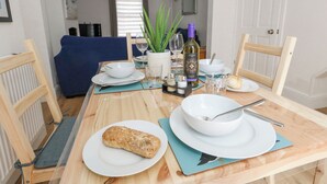 A dining table set with plates, bowls, a bottle, and a loaf of bread. - Day Cottage (Weymouth)