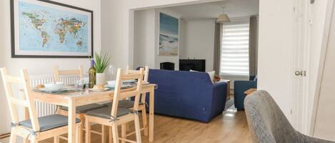 A dining area with a wooden table and chairs, a world map on the wall, and a blue sofa in the background.