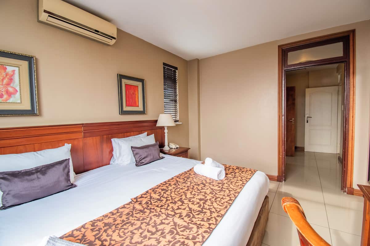 Une chambre d’hôtel avec un grand lit, une tête de lit en bois, une table de chevet avec une lampe et un tableau encadré au mur.