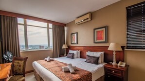 Une chambre d’hôtel avec un grand lit, deux tables de chevet, un bureau, une chaise et une vue sur la ville par la fenêtre.