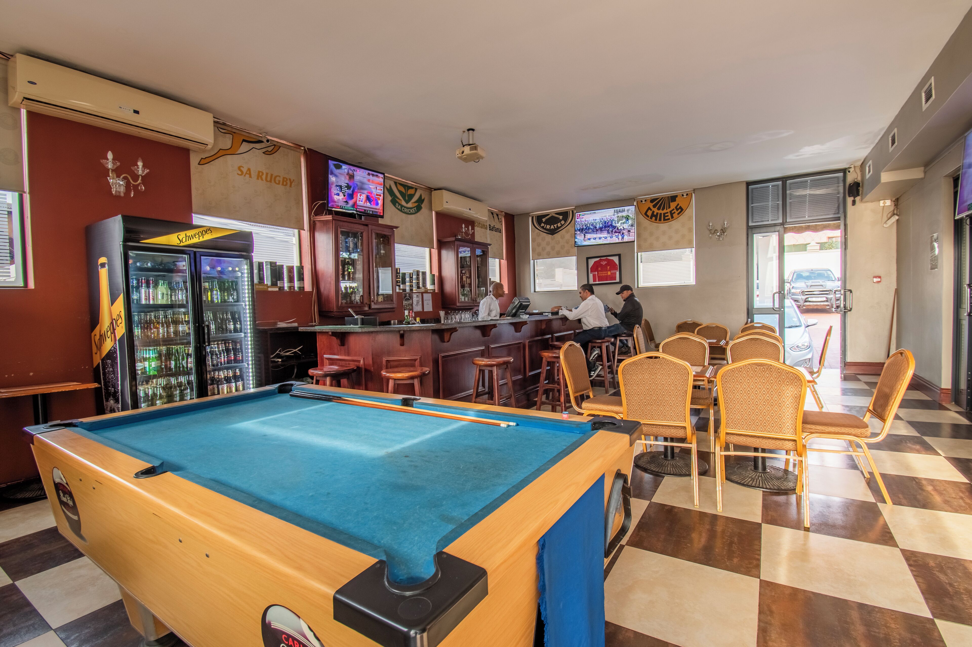 Zona de bar con mesa de billar, asientos y refrigerador lleno de bebidas.