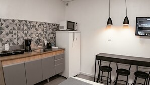 Una kitchenette compacta con microondas, cafetera y un refrigerador pequeño. Hay tres taburetes de bar y un televisor montado en la pared.