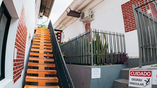 Una escalera que lleva a un edificio con una cerca metálica y un letrero que indica escalones irregulares.