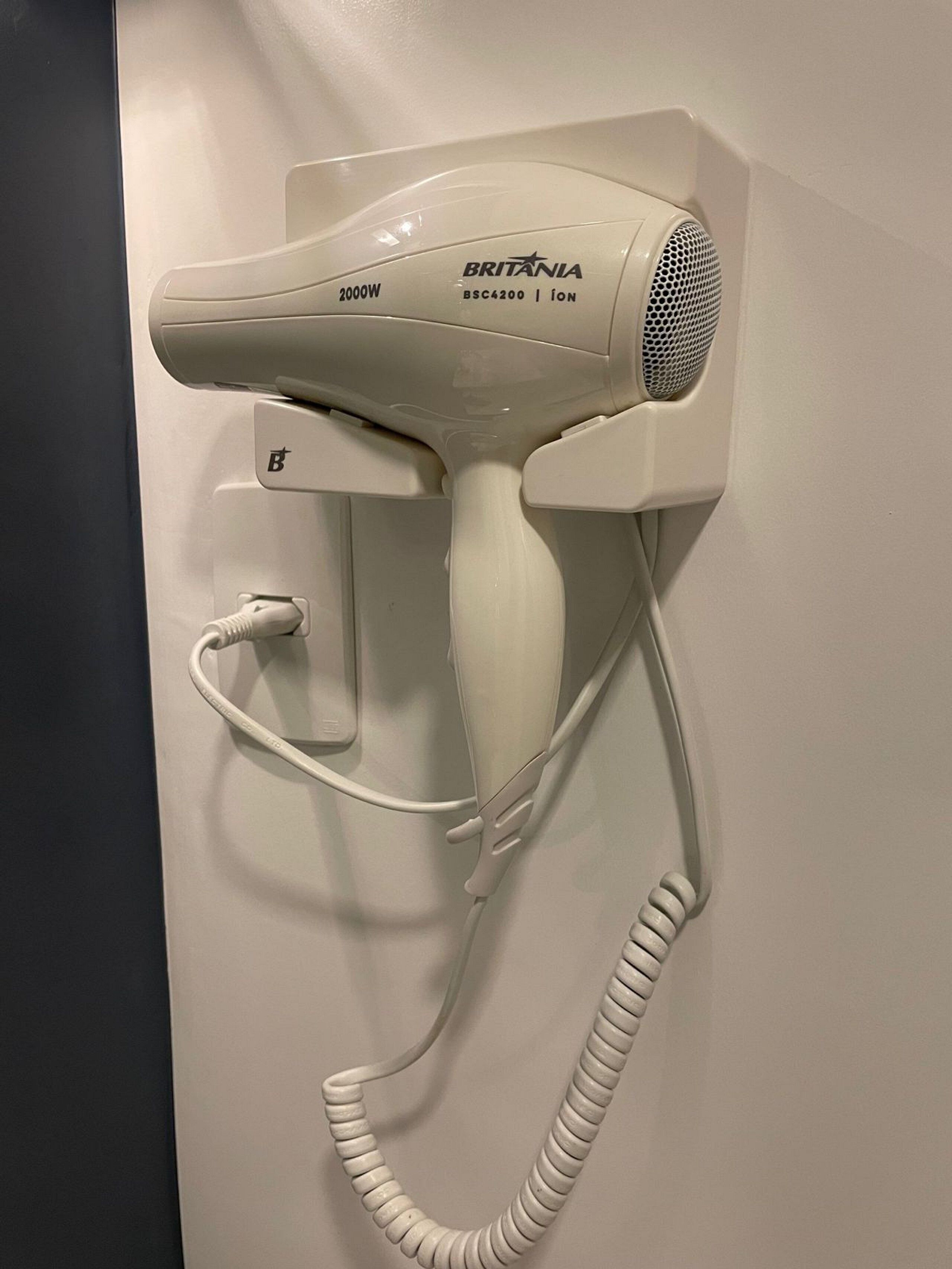 A wall-mounted hair dryer with a cord, labeled 'BRITANIA BSC4200 | ION,' and a power outlet with a plug.