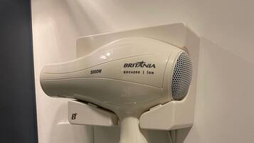 A wall-mounted hair dryer with a cord, labeled 'BRITANIA BSC4200 | ION,' and a power outlet with a plug.