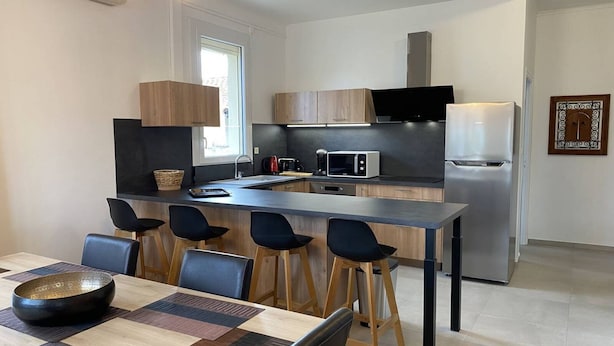 Een moderne keuken met een centraal eiland, barstoelen en een eettafel met een placemat.