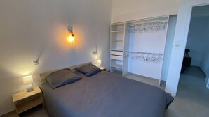 Een slaapkamer met een bed, nachtlampjes, een kledingkast en een inloopkast met hangende kleding.