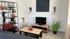 Een moderne woonkamer met een flatscreen televisie, een boekenkast, een bijzettafeltje en een kamerplant.